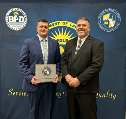 Two men in suits stand in front of a back drop that reads "Florida Leadership Academy. The man on the left is holding a certificate.