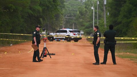 Three deputies in uniform standing on a red dirt road with crime scene tape across it.