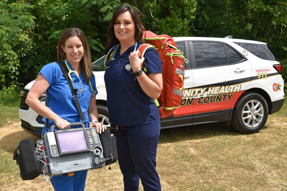 Two white female nurses wearing scrubs holding medical bags and equipment