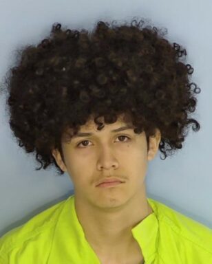 Mug shot of a hispanic male with an afro and a frown. 
