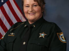 Photo of a white female wearing a deputy sheriff uniform with lieutenant bars on the collar standing in front of an American flag.
