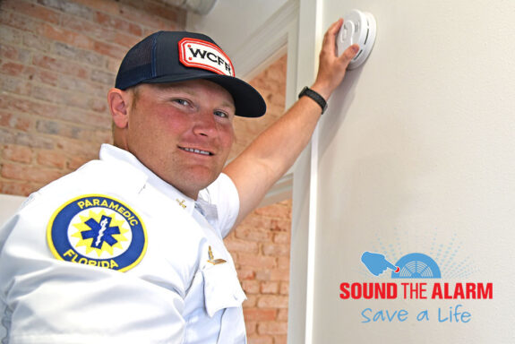 White male firefighter installing a smoke detector on a wall with a Sound the Alarm Logo