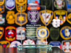 A glass award etched with writing on it and the FBI-Leeda logo sitting in front of a patch wall.