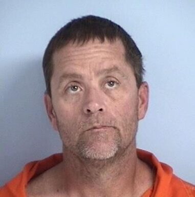 Mug shot of a white male with brown hair and blue eyes wearing an orange jumpsuit.