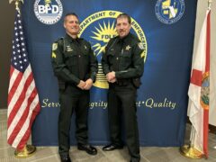 Two sheriff deputies, two men, stand in front of the American flag and the Florida flag.