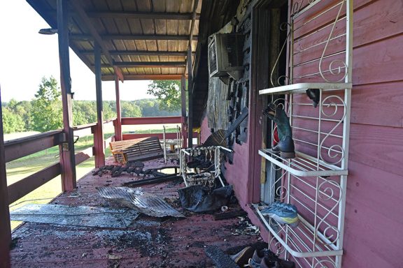 Broken glass and fire damage on the porch of an apartment above a large red barn