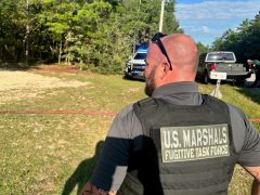 White male US Marshals Task Force Officer wearing a black bullet proof vest