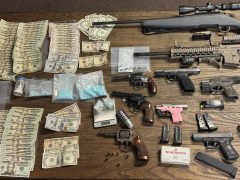 Money, guns, and drugs laid out on a wood table.