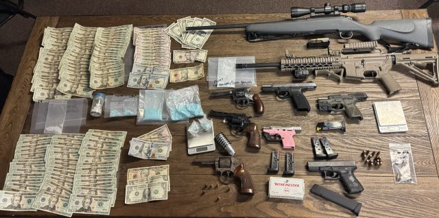 Money, guns, and drugs laid out on a wood table.