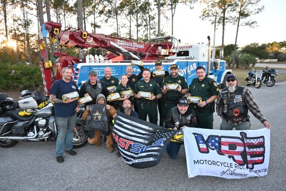 A group of deputies and motorcycle riders holding up LifeVac devices in front of a tow truck.