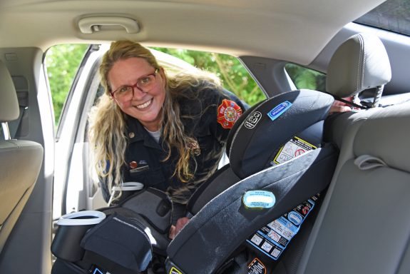 White female paramedic installing a baby car seat in the backseat of a car