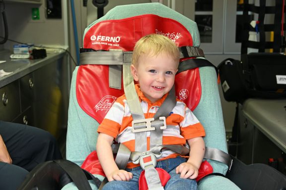 Little boy on a stretcher with a red pediatric transport device.