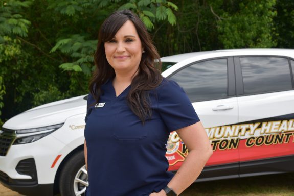 A white female with dark brown hair wearing navy blue scrubs