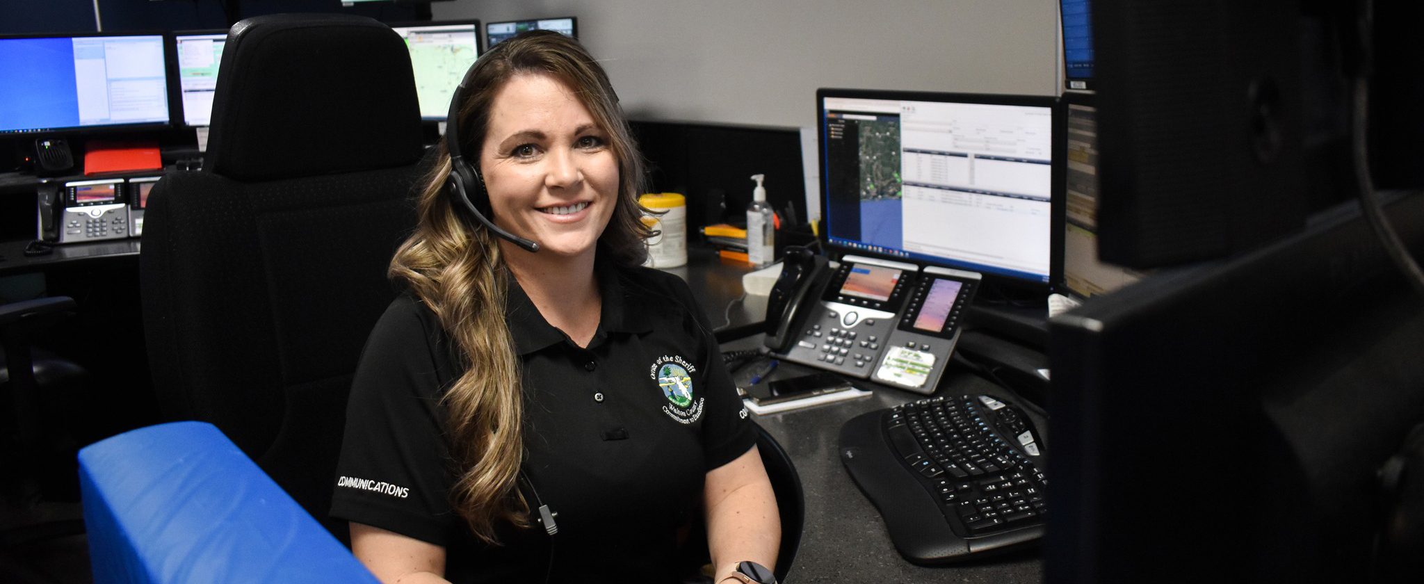 White female dispatcher sitting in a communications center wearing a headset
