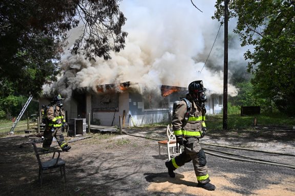 Firefighters walking in front of a large house fire