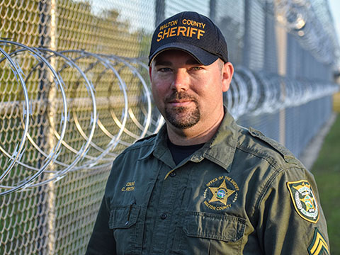 White male detention deputy standing next to jail fence with metal wiring