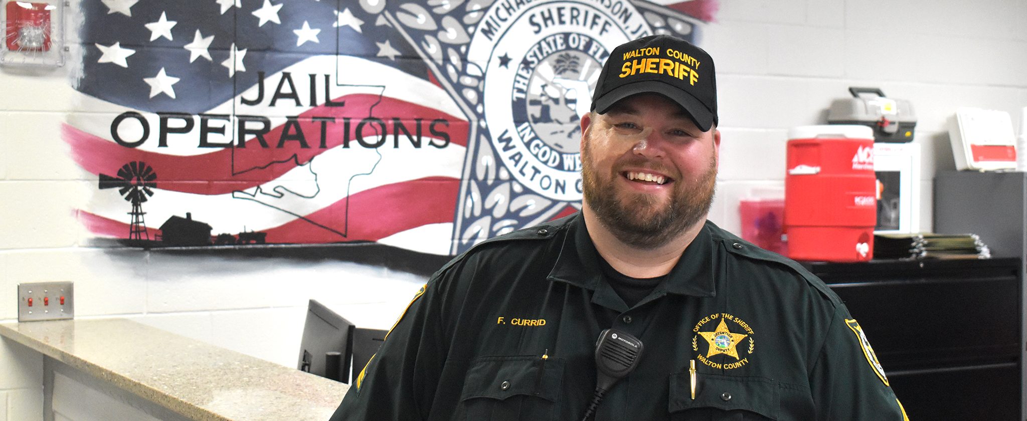 White male with birthmark on face standing in front of a wall that says "Jail Operations"