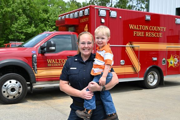 Female paramedic holding a little boy in front of a red ambulance.