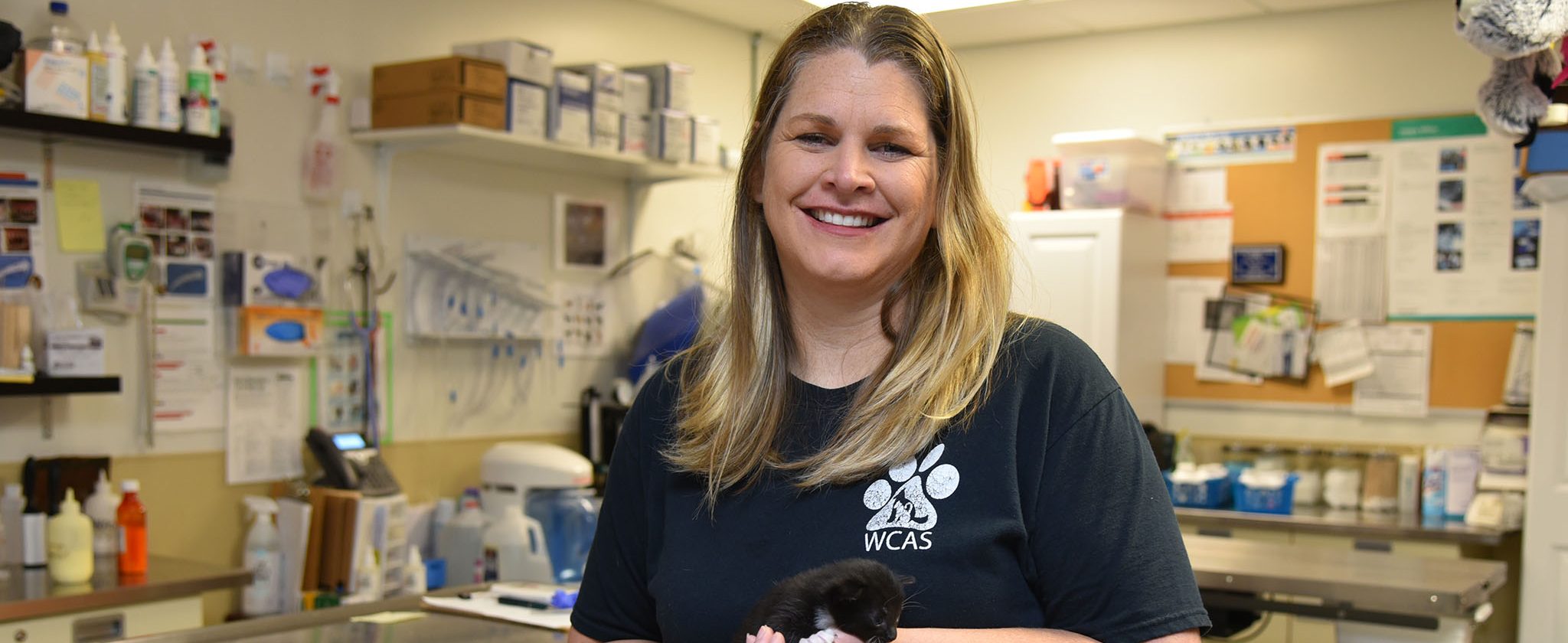 White female wearing a black animal shelter shirt holding a small black kitten