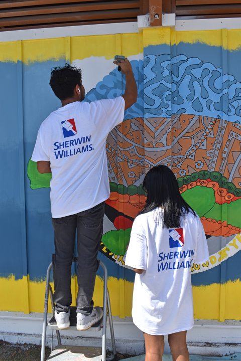 Male and female teenagers painting a colorful mural on a wall