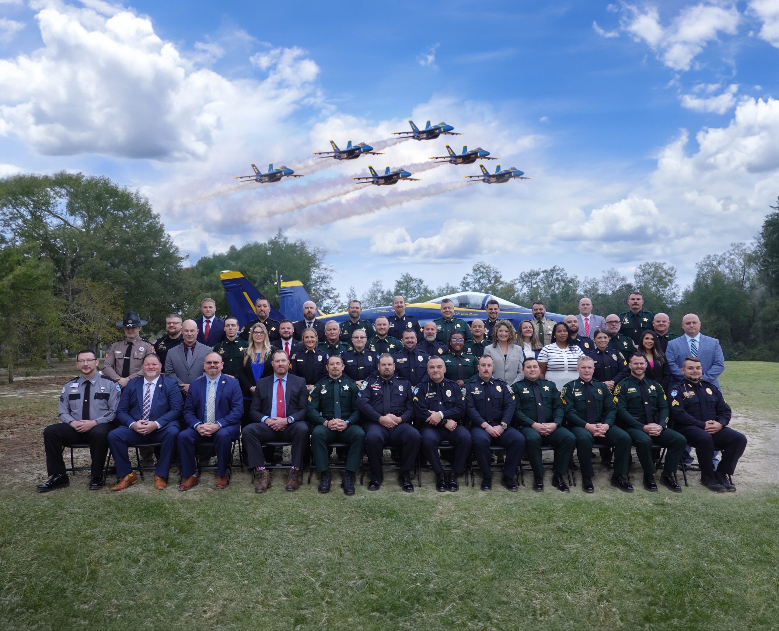 A group of law enforcement professionals in their uniforms with the Blue Angels flying in formation overhead.
