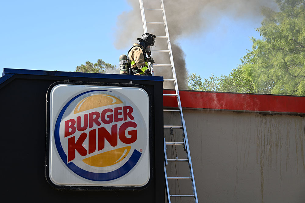 Firefighter on the roof of a Burger King building with heavy smoke coming out of the roof