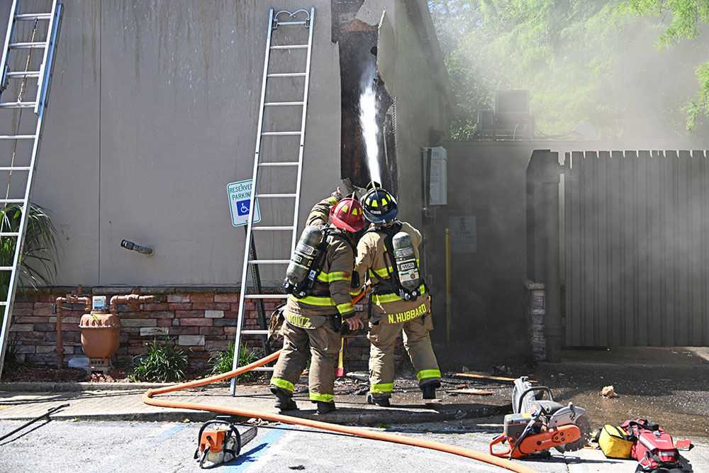 Firefighters spraying water into a large hole on the exterior wall of a Burger King