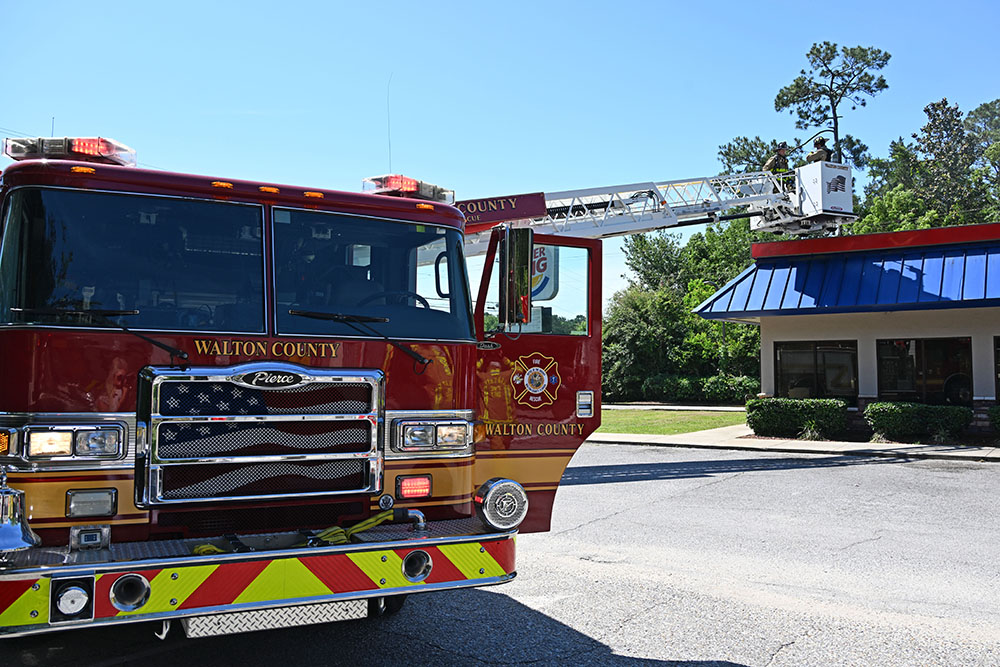 Ladder truck with a ladder extended over the roof of a burger king with two firefighters in the bucket at the end of the ladder