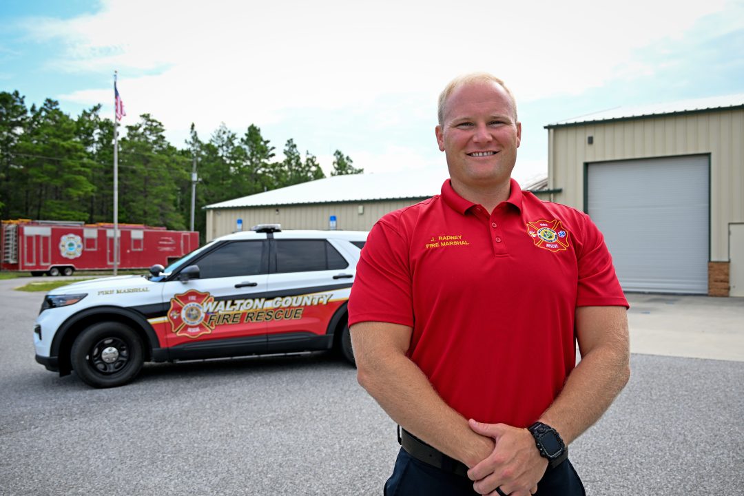 White male wearing a red polo shirt standing in front of a fire marshal vehicle