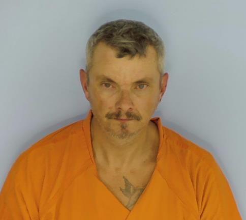 White male with light brown hair and a goatee wearing an orange jumpsuit