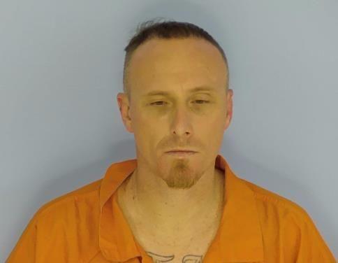 White male with short brown hair and a light brown goatee wearing an orange jumpsuit