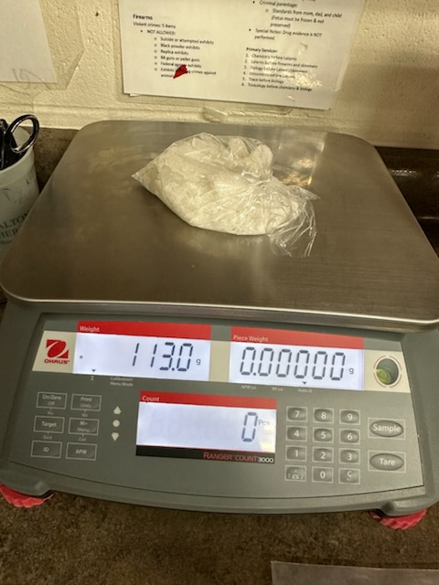A scale reading "113" with a plastic bag on top with a white powdery substance inside.