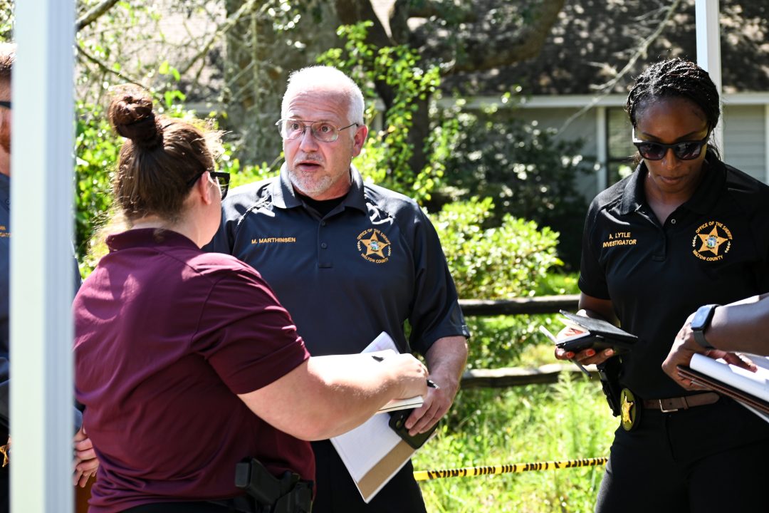 A white male with white hair and a sheriff's office polo standing next to an African American female with a Walton County Sheriff's Office polo holding notepads