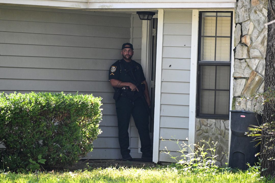 A deputy sheriff holding an AR stands at the front door of a residence.