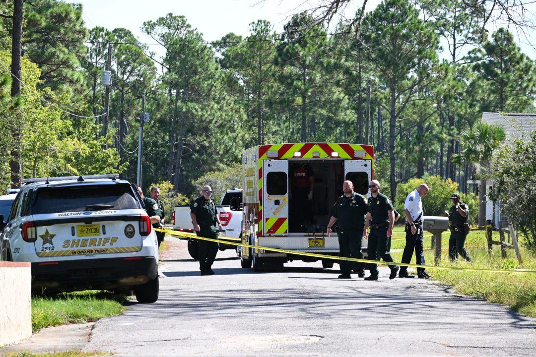 Deputies and Firefighter EMTs stand near an ambulance with crime scene tape in the foreground.