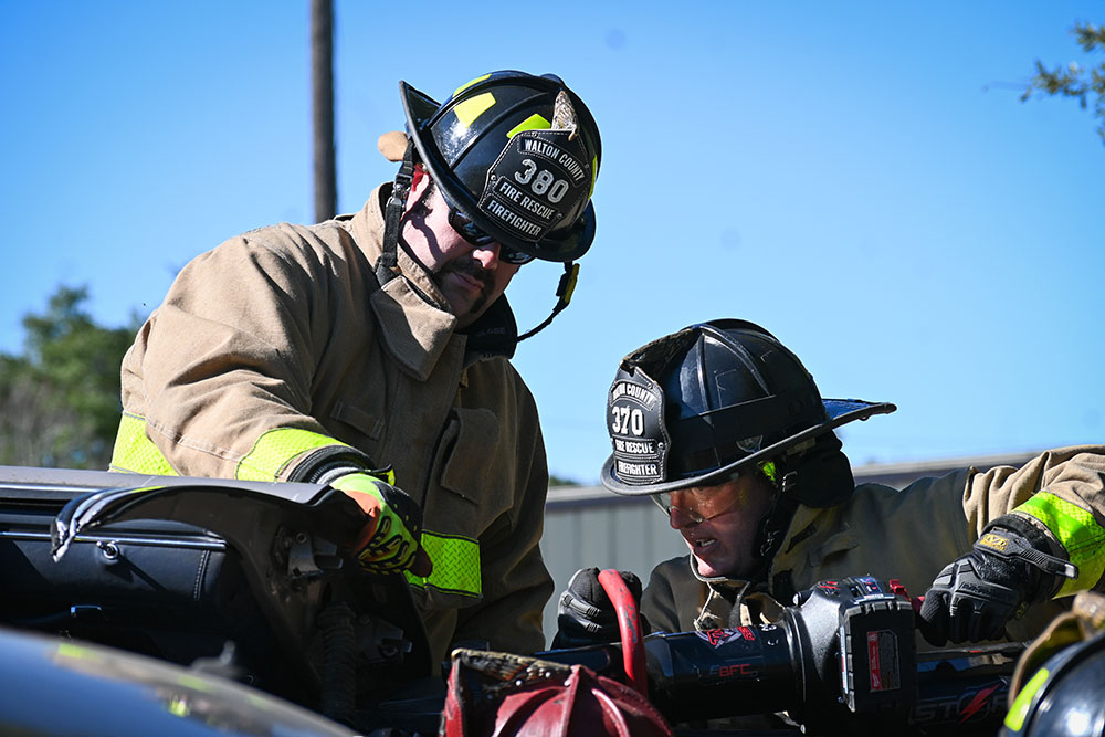 Two male firefighters performing extrication on a car