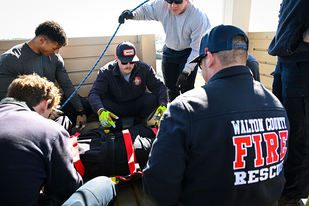 Group of male firefighters huddled around a firefighter being strapped into a gurney 