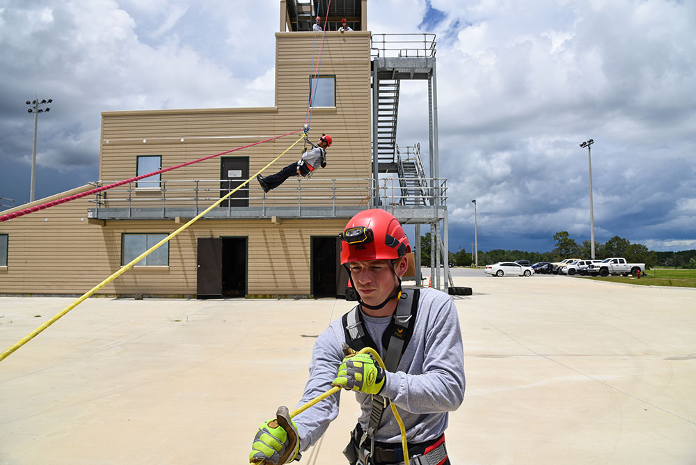 Young male firefighter pulling a rope while another firefighter slides down the rope from a fire tower
