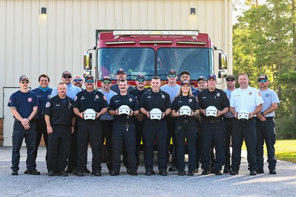 Male and female firefighters standing in front of a fire truck holding white technical rescue helmets