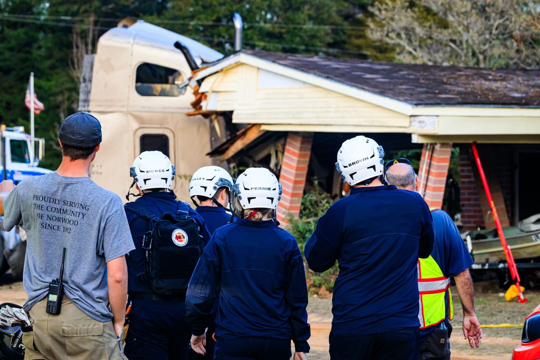 Firefighters wearing white helmets walking towards the scene of a semi that crashed into a home