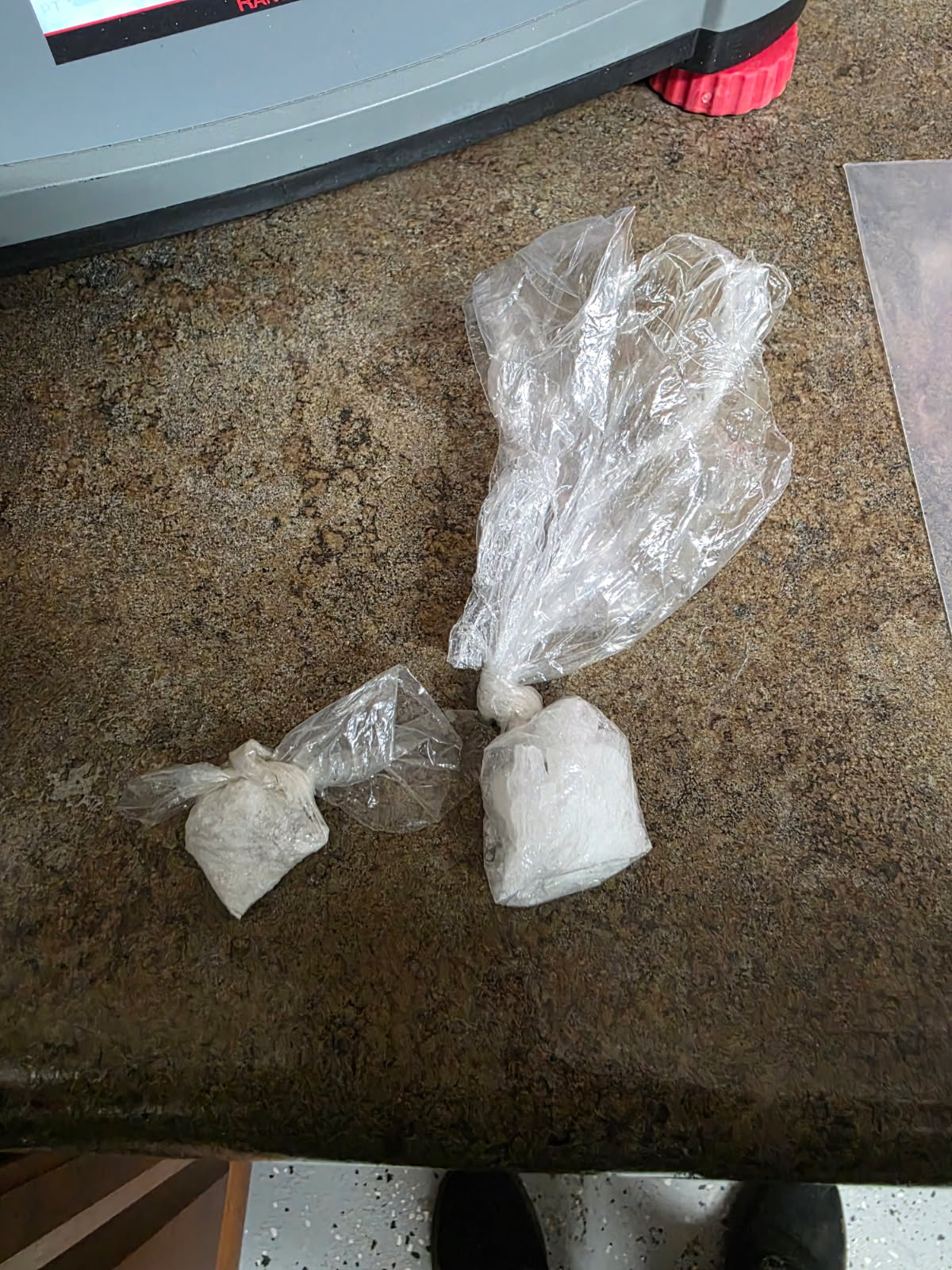 Two clear plastic bags containing a white powdery substance lying on a stained concrete floor near a piece of equipment