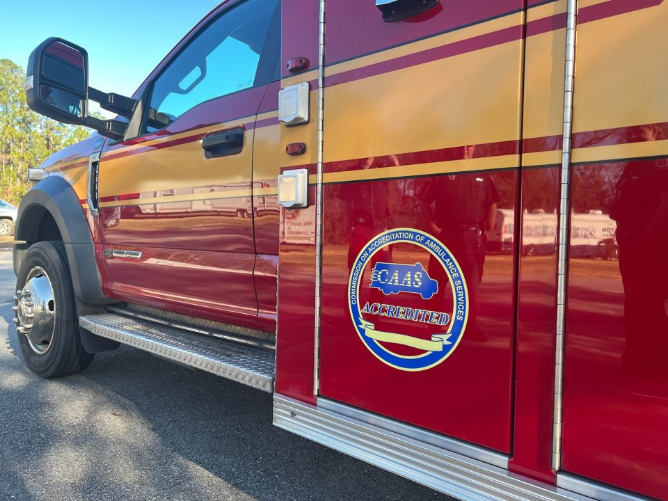 Red ambulance with gold stripe down the side and a large CAAS accreditation sticker behind the driver door.