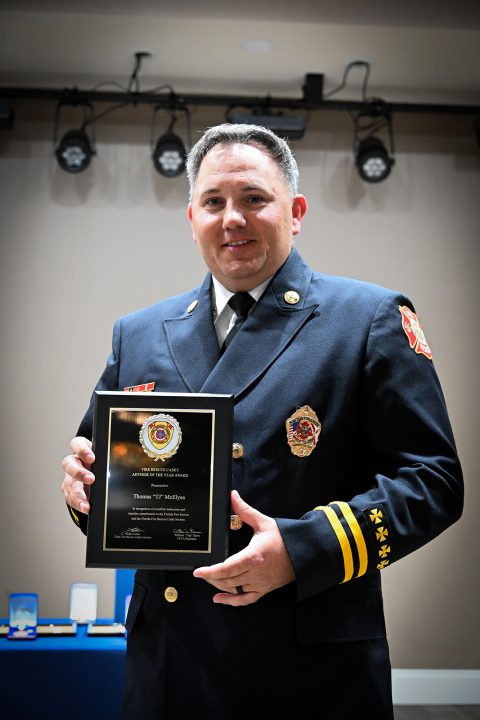 White male battalion chief in a navy blue uniform holding an award