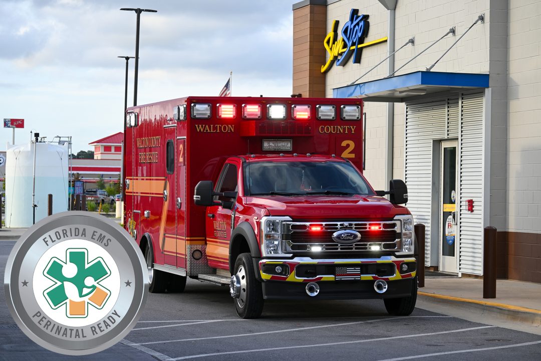 Red ambulance with flashing red and white lights parked in front of a Sun Stop gas station with a Florida EMS Perinatal Ready logo on the photo