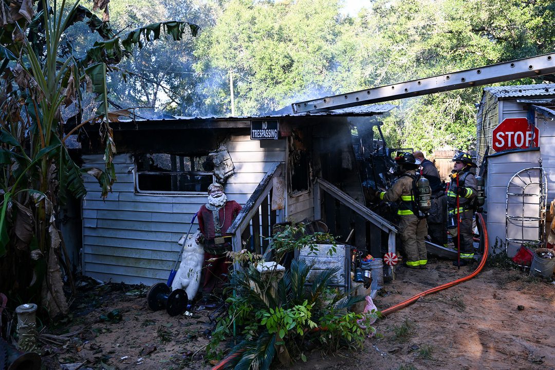 Firefighters standing outside of a shed with smoke coming out of the top of it.