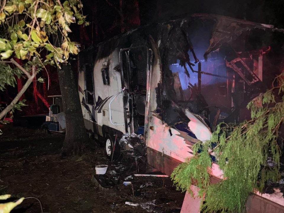 Night photo of a white camper with severe fire damage on the inside of the vehicle
